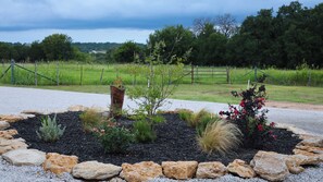 A landscaped garden with a variety of plants, a decorative wooden planter, and a gravel border. - 3-bedroom+office luxury home on the edge of GlenRose, TX. Private. Pickleball. (Rainbow)