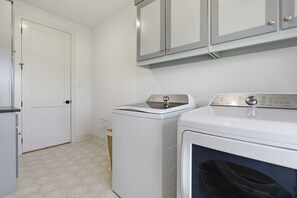 A laundry room with two washing machines, a white door, and a patterned floor. - 3-bedroom+office luxury home on the edge of GlenRose, TX. Private. Pickleball. (Rainbow)