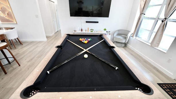 A pool table with a cue stick and balls, a television mounted on the wall, and a window with curtains. - 3BR Hollywood Home nr Hard Rock, Beach & FLL (Hollywood)