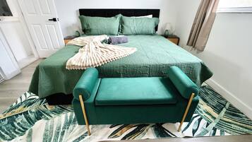 Un dormitorio ordenado con cama, mesita de noche y una silla tapizada en verde.