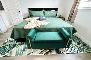 Ein ordentlich eingerichtetes Schlafzimmer mit Bett, Nachttisch und einem grünen, gepolsterten Sessel.