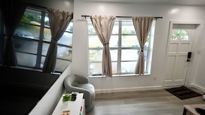 A modern room with a sofa, a small table with a plant, a window with curtains, and a door. - 3BR Hollywood Home nr Hard Rock, Beach & FLL (Hollywood)