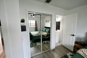 Slaapkamer met een schuifdeurkast, een bed met groene beddengoed, een nachtkastje met een lamp en een kleine potplant.