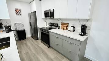 Una cocina moderna con electrodomésticos de acero inoxidable, encimera de mármol y muebles grises.