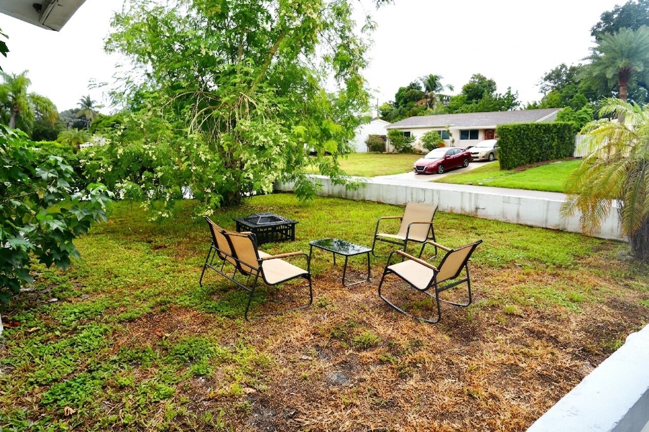 Un patio trasero con una mesa y sillas, un jardín y una casa al fondo.
