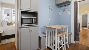A compact kitchen with a microwave, a small table with stools, and a grey cabinet. - Charming Del Ray Home, Near Old Town & METRO-rail (Alexandria)