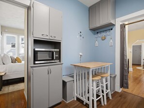 A compact kitchen with a microwave, a small table with stools, and a grey cabinet. - Charming Del Ray Home, Near Old Town & METRO-rail (Alexandria)