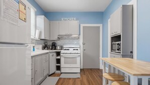 A compact kitchen with white cabinets, a stove, and a wooden table with stools. - Charming Del Ray Home, Near Old Town & METRO-rail (Alexandria)