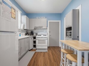 A compact kitchen with white cabinets, a stove, and a wooden table with stools. - Charming Del Ray Home, Near Old Town & METRO-rail (Alexandria)