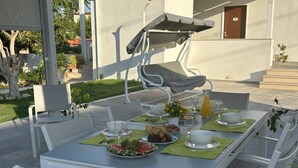 An outdoor dining area with a table set for two, surrounded by white chairs, a covered seating area, and a view of a building with steps. - A property surrounded by greenery in the center of Pompeii, across from the entrance to the archaeological site (Pompei)