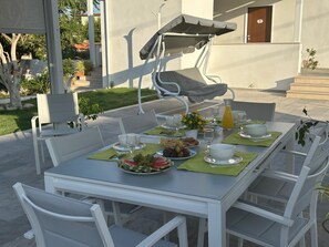 An outdoor dining area with a table set for two, surrounded by white chairs, a covered seating area, and a view of a building with steps. - A property surrounded by greenery in the center of Pompeii, across from the entrance to the archaeological site (Pompei)