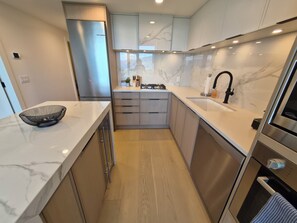A modern kitchen with marble countertops, stainless steel appliances, and wooden cabinets. - Aqua Oasis Beach Club Resort 2.0 - Located right on the beach. (Kelowna)