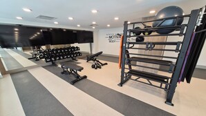 Ein Fitnessraum mit Trainingsgeräten, einem an der Wand montierten Fernseher und einem Motivationsposter.
