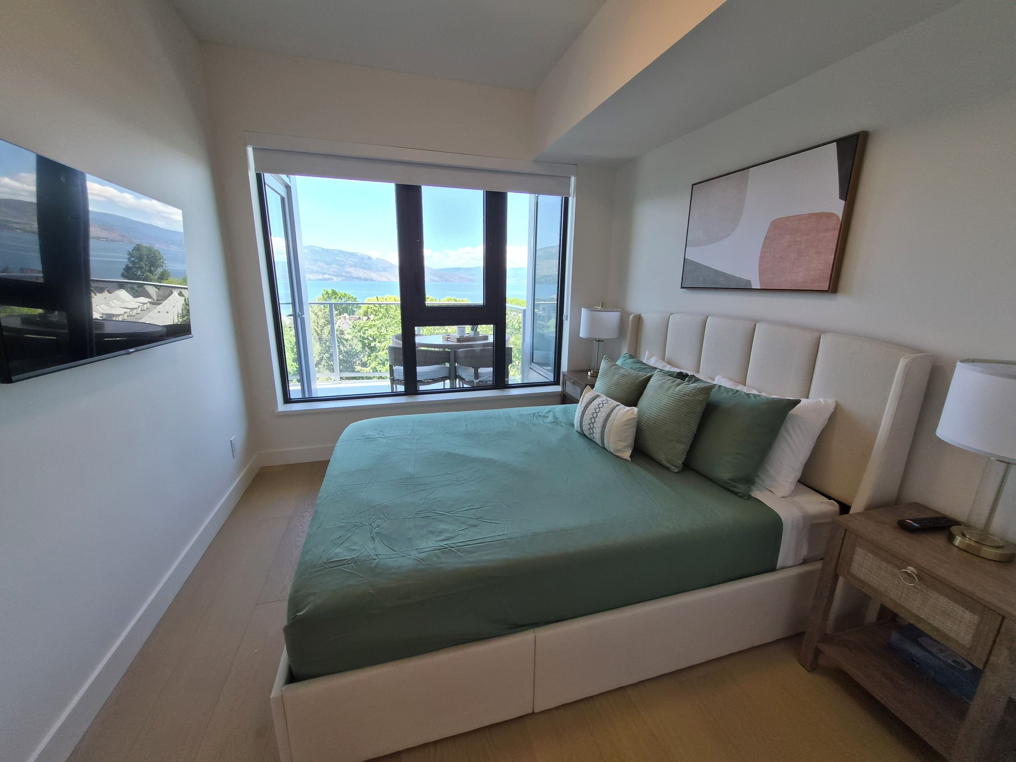 Ein Schlafzimmer mit einem großen Bett, einem Nachttisch, einem Fernseher und einem Balkon mit Blick.