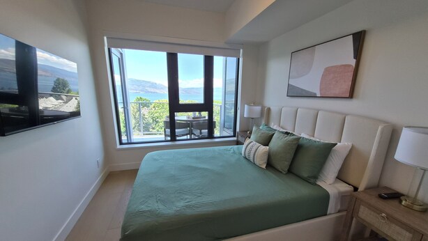 Ein Schlafzimmer mit einem großen Bett, einem Nachttisch, einem Fernseher und einem Balkon mit Blick.