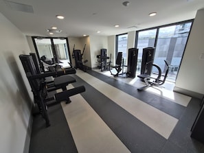 Ein Fitnessstudio mit verschiedenen Trainingsgeräten, einer Bank und großen Fenstern.
