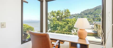 Una habitación con escritorio, silla y vista a un cuerpo de agua y vegetación.