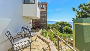 A balcony with a table and chairs, a small garden, and a view of the sea. - Coastal Sanctuary: Newly Remodeled, Unrivaled Views, Sauna, and Steps to Ferry! (Sausalito)