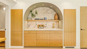 A modern kitchen with wooden cabinets, a marble countertop, and a tiled backsplash. - Coastal Sanctuary: Newly Remodeled, Unrivaled Views, Sauna, and Steps to Ferry! (Sausalito)
