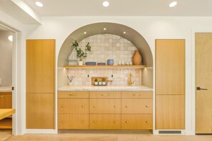 A modern kitchen with wooden cabinets, a marble countertop, and a tiled backsplash. - Coastal Sanctuary: Newly Remodeled, Unrivaled Views, Sauna, and Steps to Ferry! (Sausalito)