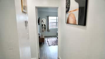 Un pasillo con una puerta que da a una habitación, un espejo, una ventana con cortinas y una obra de arte enmarcada en la pared.