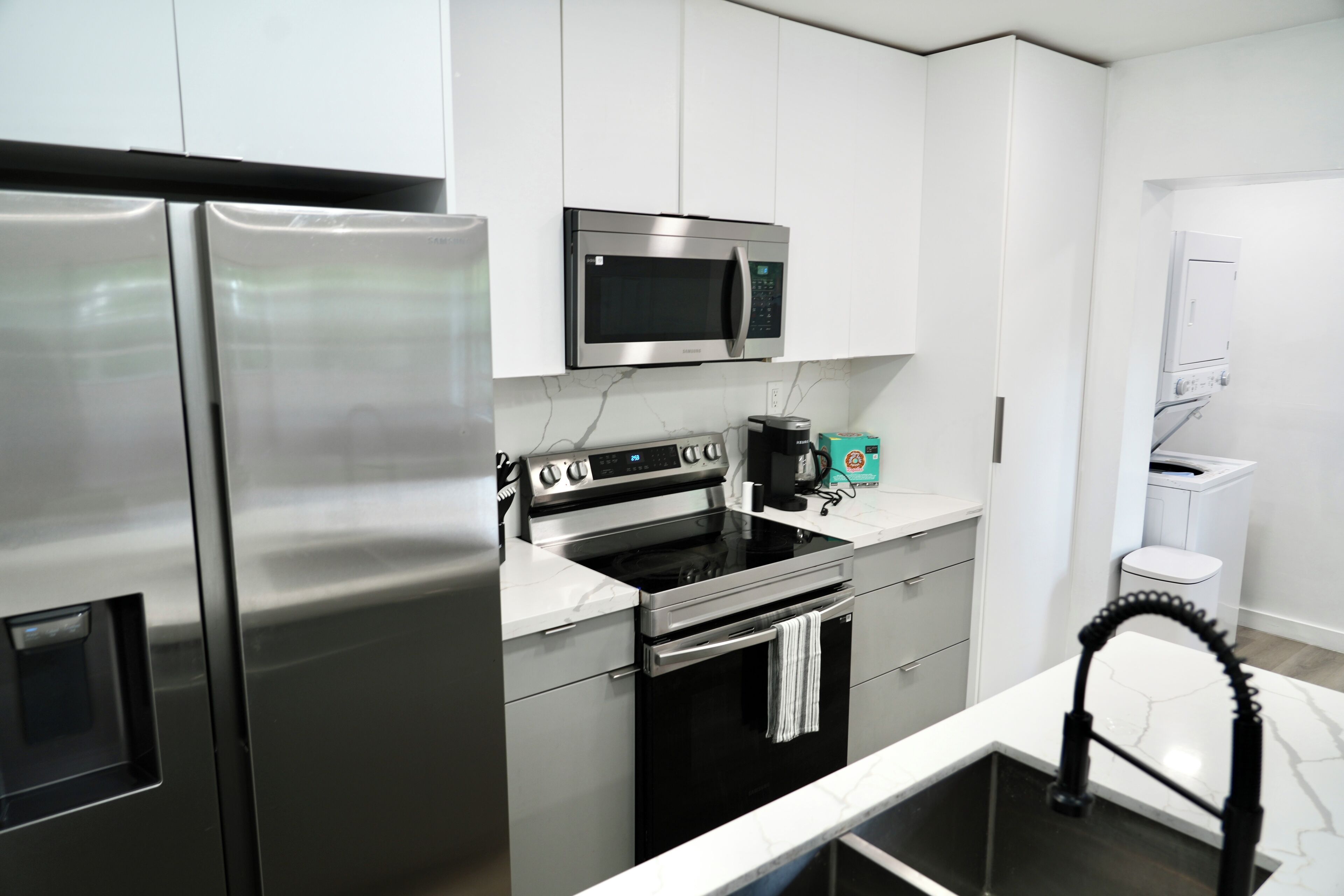Una cocina moderna con electrodomésticos de acero inoxidable, incluyendo un refrigerador, microondas, horno y cafetera.