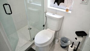 Kylpyhuone, jossa on wc, lasinen suihkuseinä, ikkuna, josta on näkymä, ja pieni hylly, jossa on hygieniatuotteita.