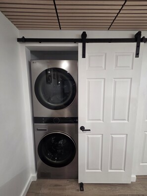 A laundry room with two stacked washing machines, a sliding door, and a wooden ceiling. - Centrally located 1-bedroom apartment close to downtown Wifi AC washer/dryer (Twin Falls)