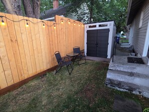 A wooden fence with string lights, a black gate, and a small patio with two chairs and a table. - Centrally located 1-bedroom apartment close to downtown Wifi AC washer/dryer (Twin Falls)