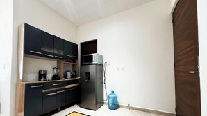 Eine kleine Küche mit dunklen Schränken, einem Kühlschrank und einem Wasserspender.