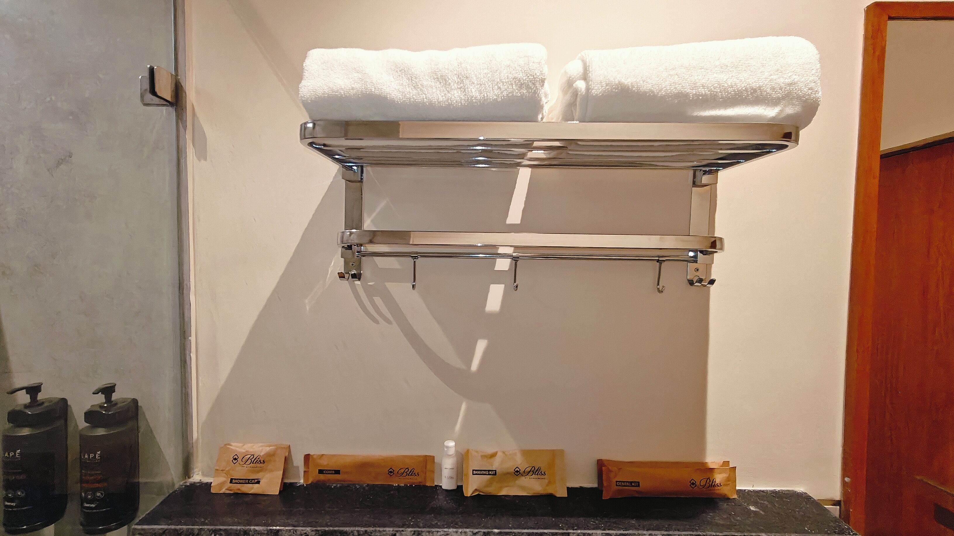 A bathroom with a towel rack holding two white towels, a shower caddy with toiletries, and a door to the right.