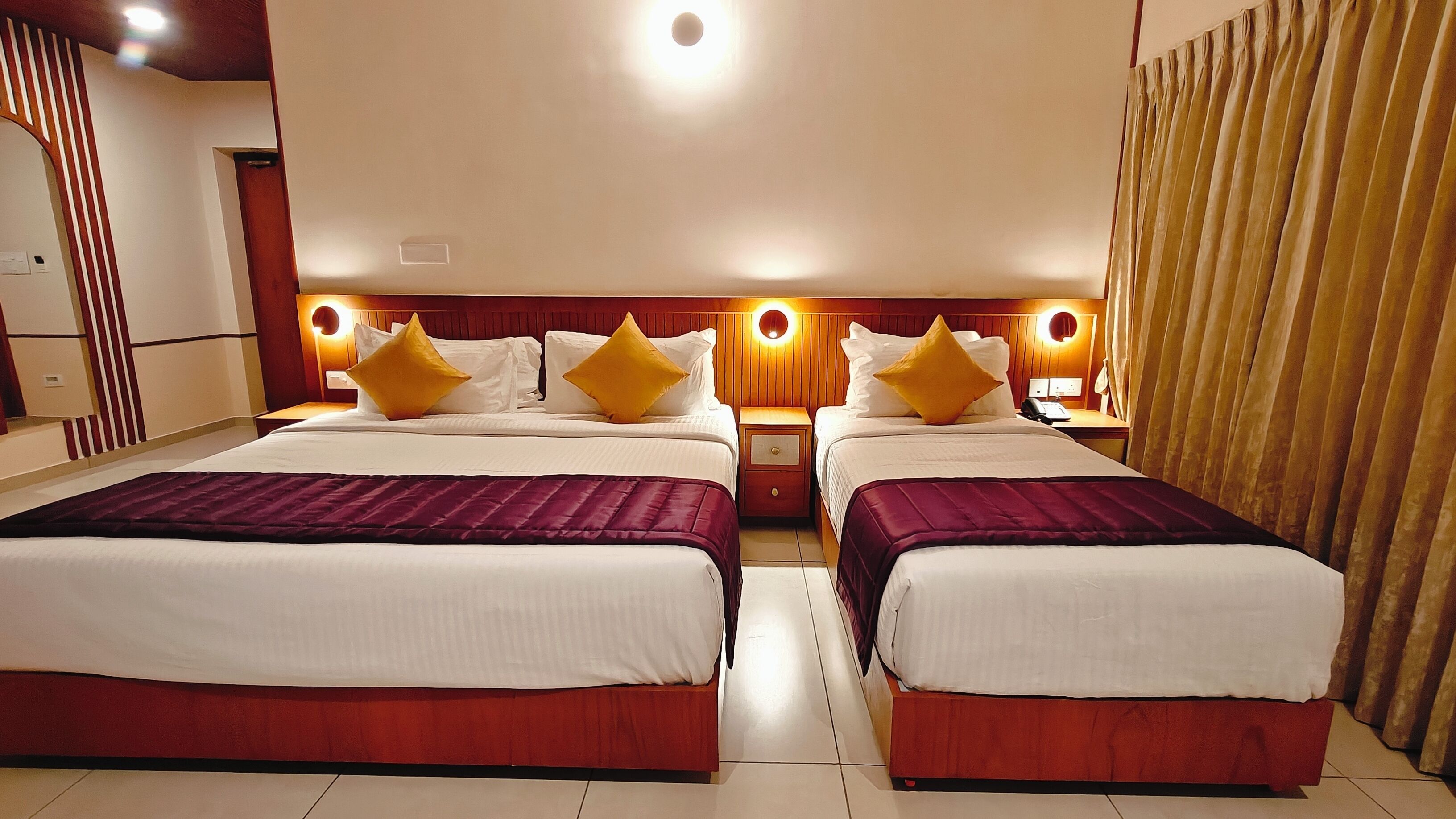 Ein Hotelzimmer mit zwei Betten, jeweils mit roter Bettdecke, weißen Laken und gelben Kissen. An den Nachttischen stehen Lampen und ein Spiegel.