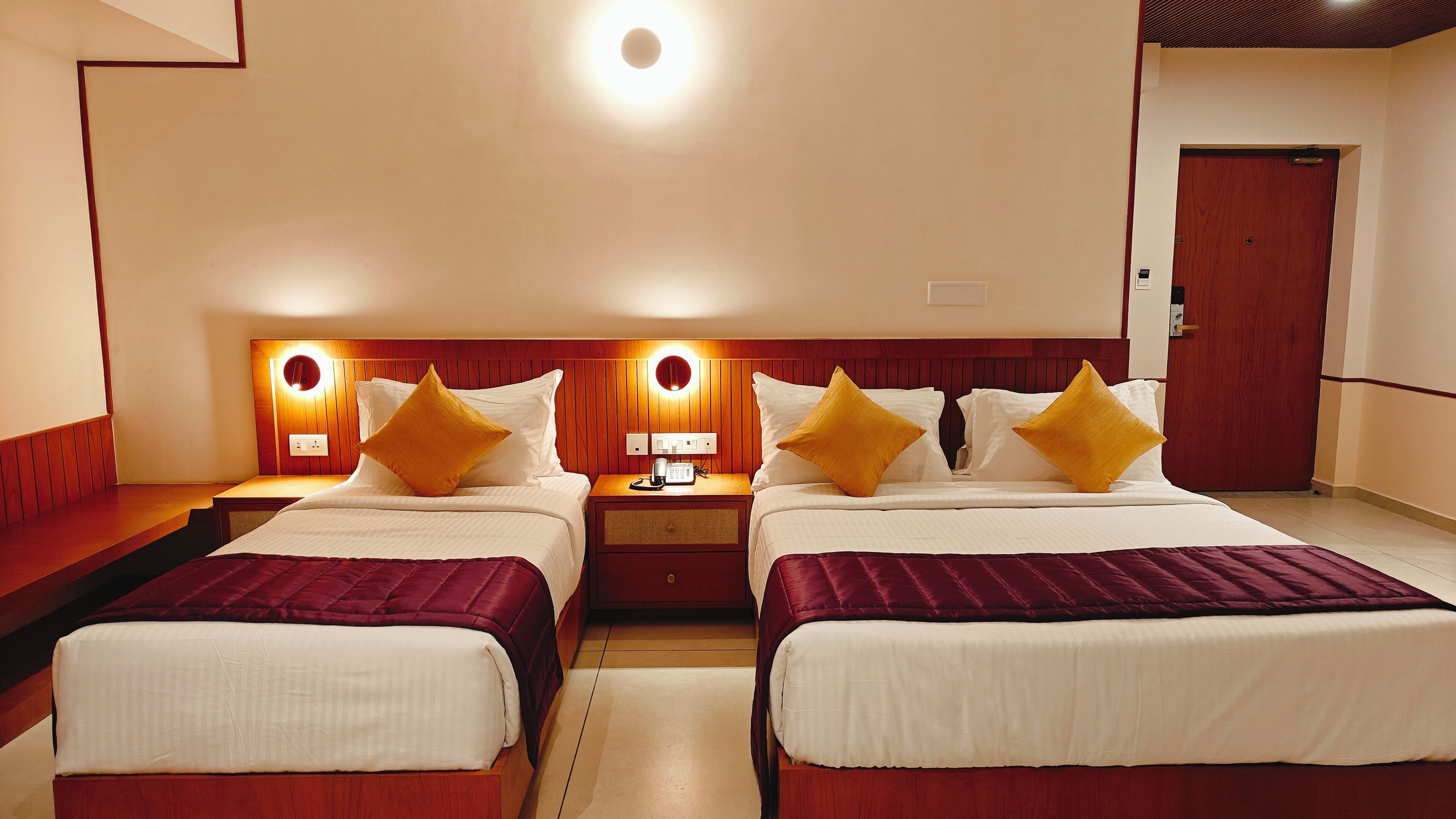Een hotelkamer met twee bedden, elk voorzien van een rode sprei, een nachtkastje met een lamp en een wandlamp.