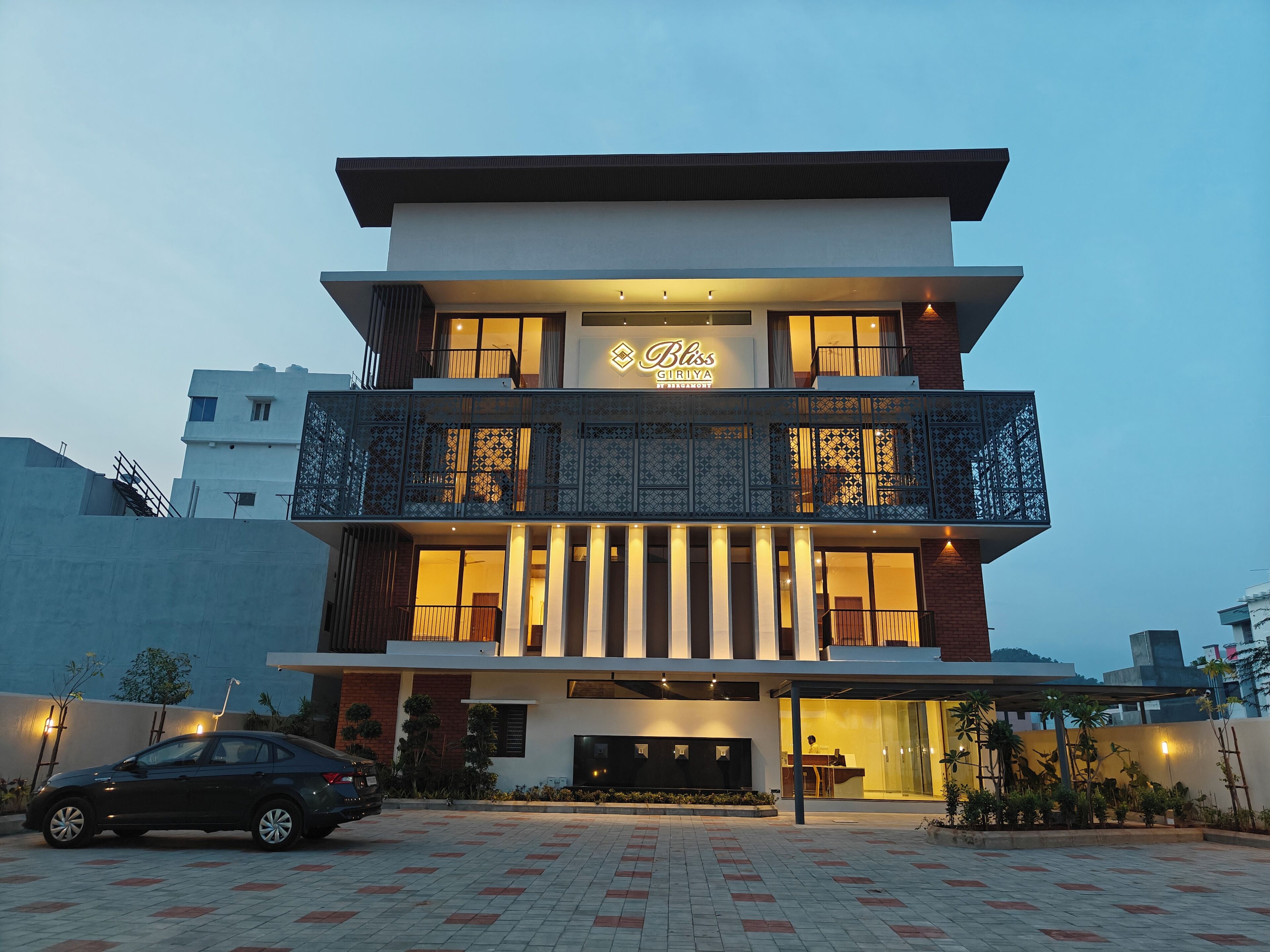 Een modern hotel met een tweetal verdiepingen, een balkon met decoratieve hekwerk en een bord met de naam 'Bliss Giriya'.