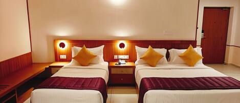 A hotel room with two beds, a bedside table with a lamp, a phone, and a wall-mounted light fixture.