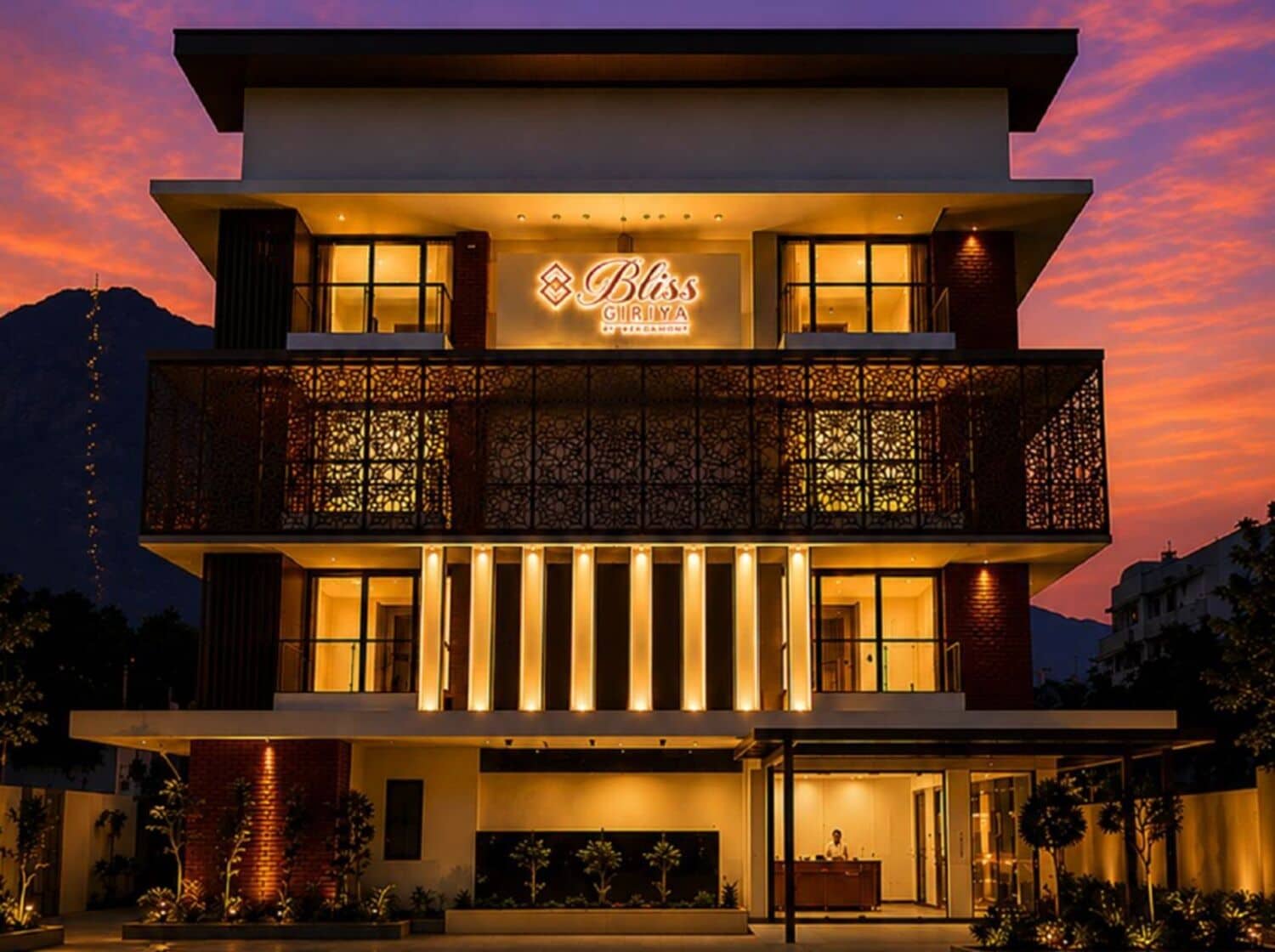 A modern hotel with a prominent sign, a balcony with intricate lattice work, and a well-lit entrance.