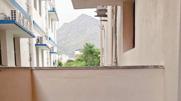 Rincón de una habitación de hotel con una mesa de madera, vista a una montaña y un edificio con detalles azules.