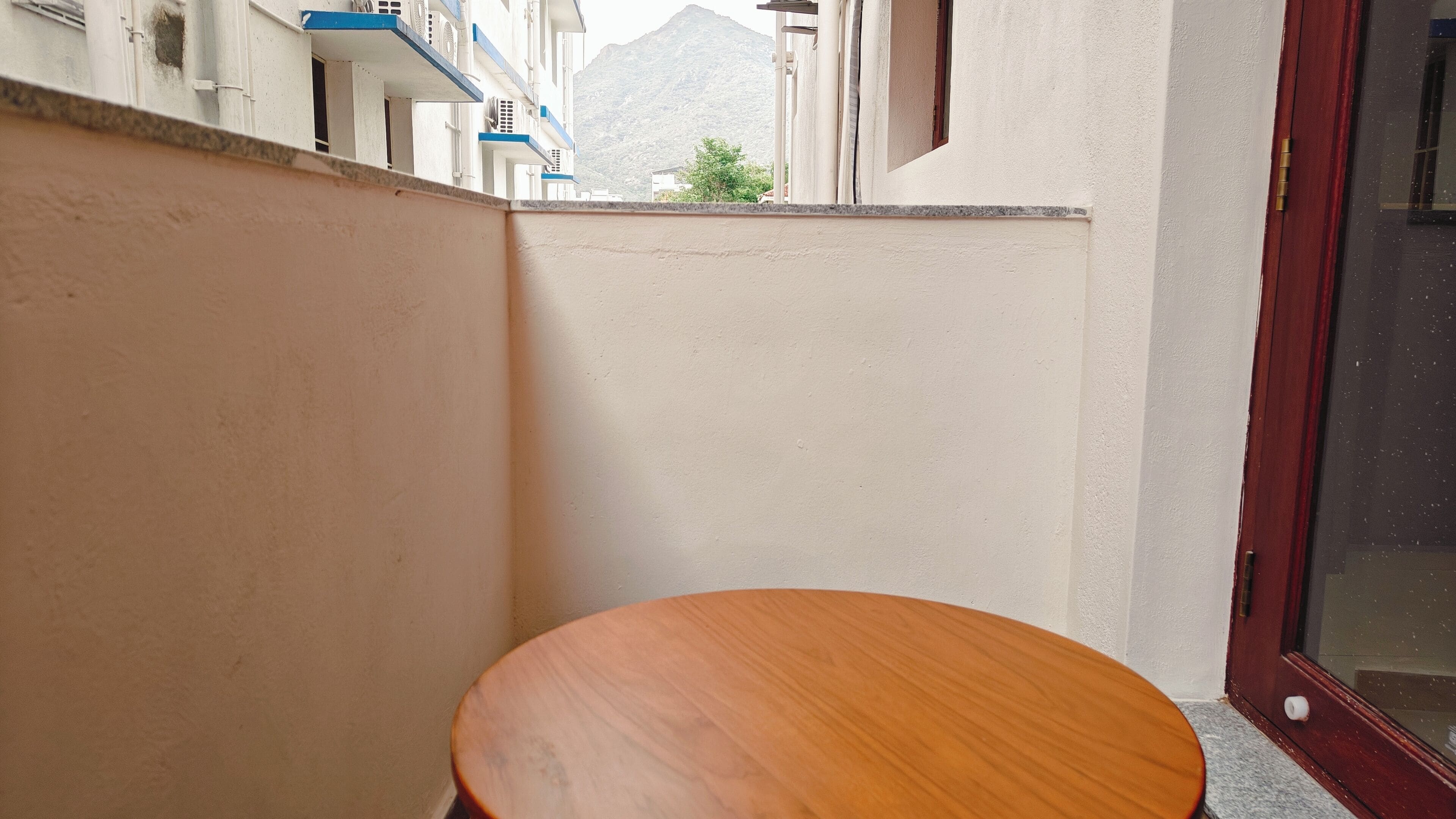 A corner of a room with a wooden table, a white wall, and a view of a mountain.