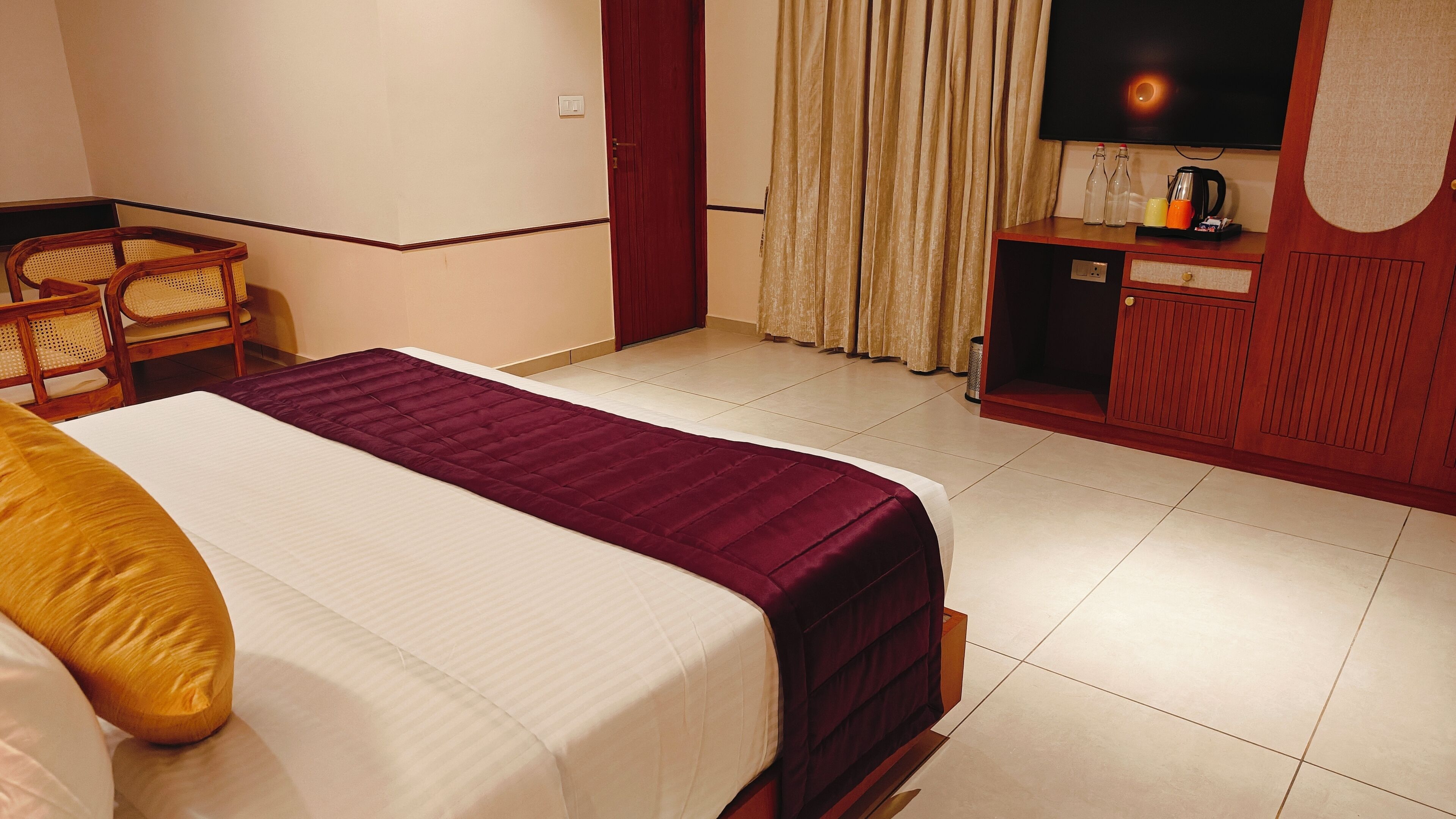 Ein Hotelzimmer mit einem Bett, einem Holzsessel, einem Fernseher und einer Minibar.