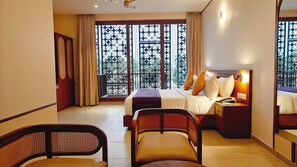 A hotel room with a bed, bedside table, lamp, and a view through a window with decorative metal grilles. - Bliss Giriya By Bergamont (Tiruvannamalai)