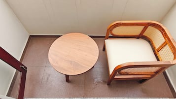 A small room with a round wooden table and a wicker chair with a white cushion.