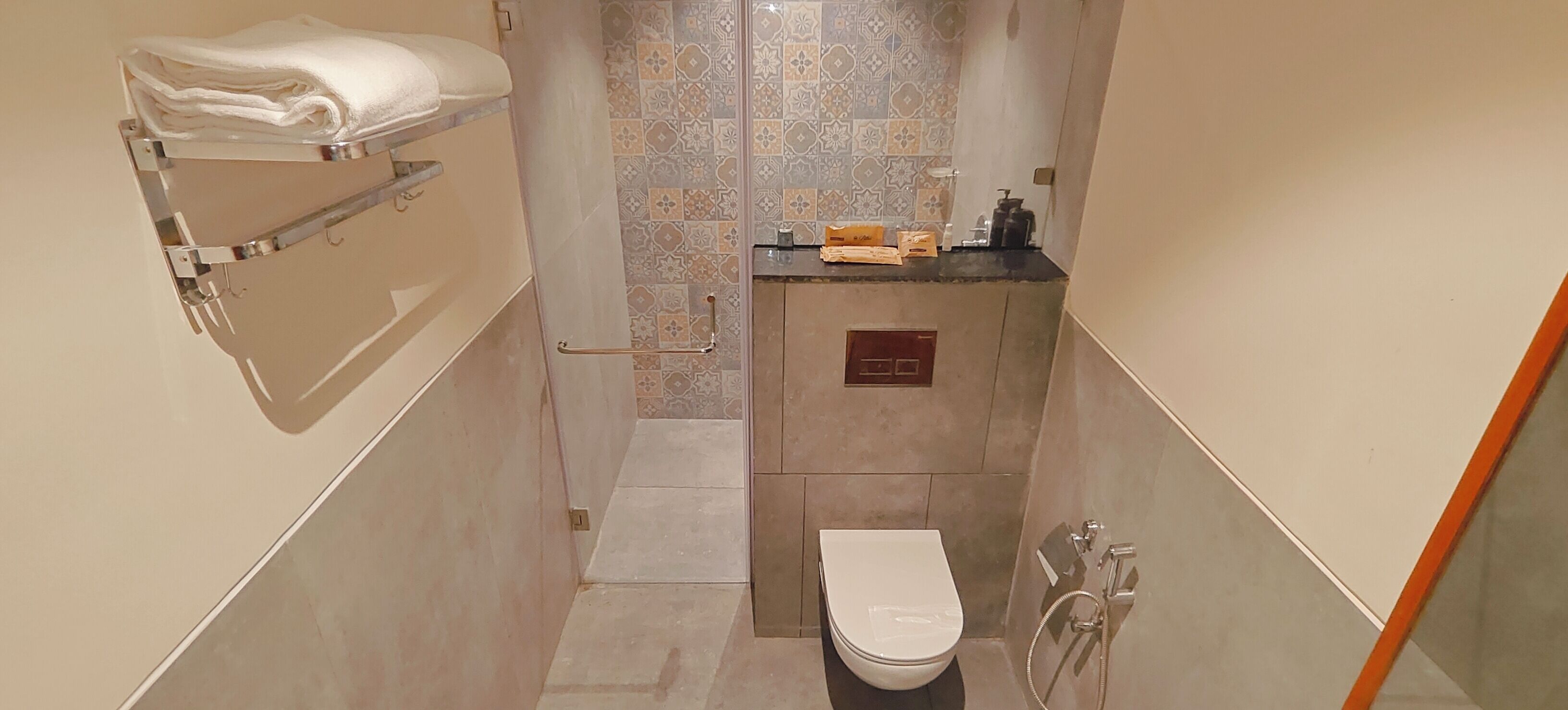 Ein schmales Badezimmer mit Toilette, Handtuchhalter und Duschbereich.