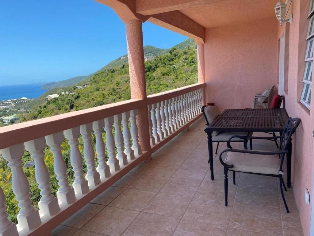 Un balcón con una mesa y sillas, con vistas a un paisaje escénico de colinas y el mar.