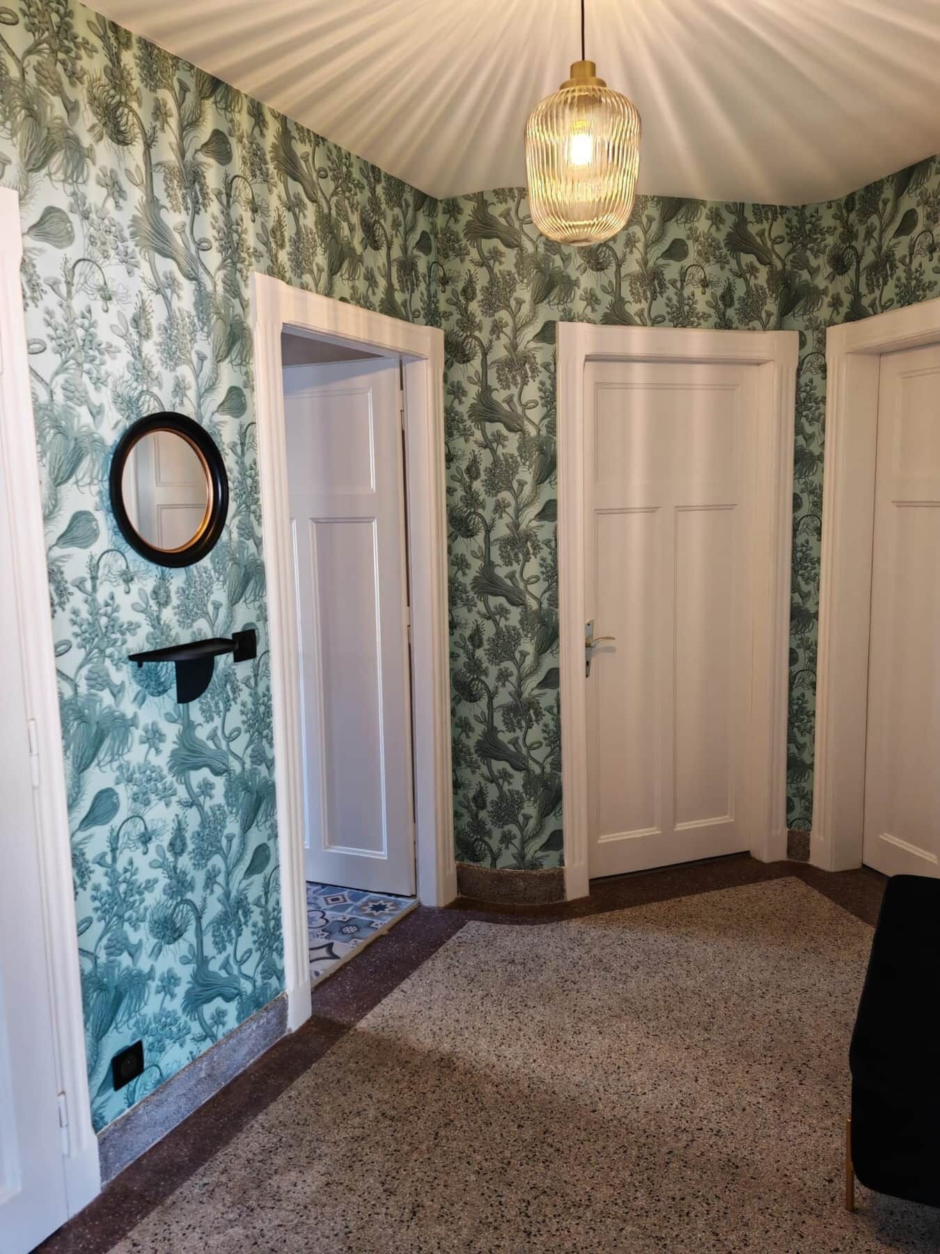Ein Flur mit floralem Wandpapier, weißen Türen, einer hängenden Leuchte und einem Spiegel an der Wand.