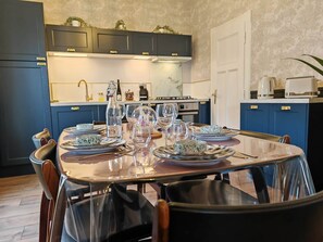 A dining area with a table set for four, kitchen cabinets, a stove, and a sink in the background. - The Vintage: A 4-Star Apartment for up to 5 People (Metz)