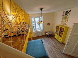 Ein Zimmer mit einem Bett, einem Fenster, einer Heizung, einem kleinen Tisch und einem gelben Schrank.