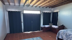 Ein Schlafzimmer mit einem Bett, einer Sitzbank, einem Fenster mit Vorhängen und einem Fliesenboden.