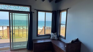Ein Zimmer mit einer großen Schiebeglaswand, die auf einen Balkon mit Blick aufs Meer führt. An der Wand steht eine Holzbank mit Kissen.
