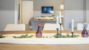 Ein modernes Wohnzimmer mit einem Holztisch, weißen Sofas, einem Flachbildfernseher und einem dekorativen Mittelstück mit Kerzen und einer Vase.