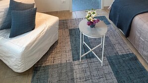 Een knus interieur met een bed, een tafeltje met een vaas en een raam met gezoet glas.